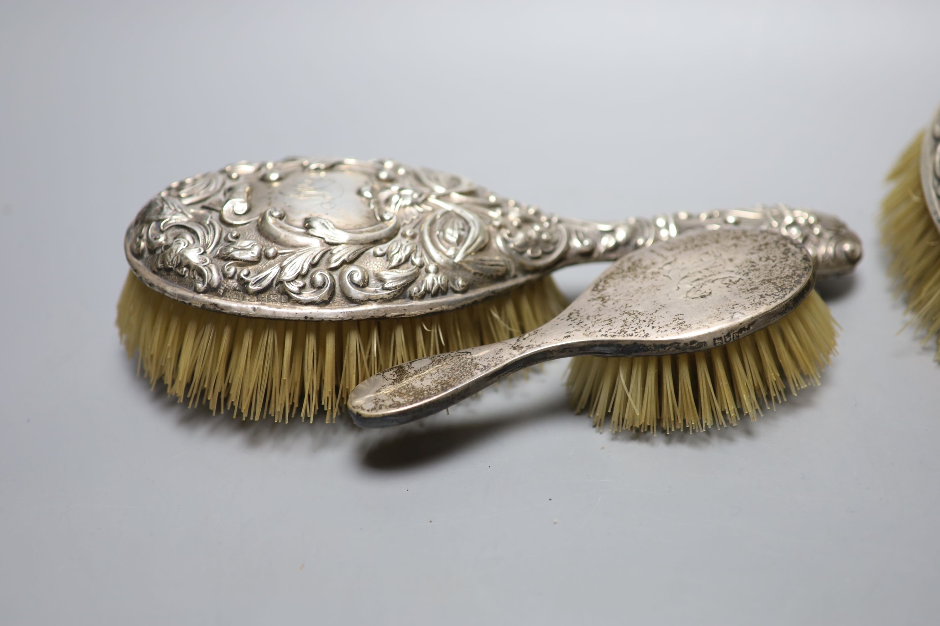 A pair of Edwardian repousse silver backed hair brushes and two other brushes.